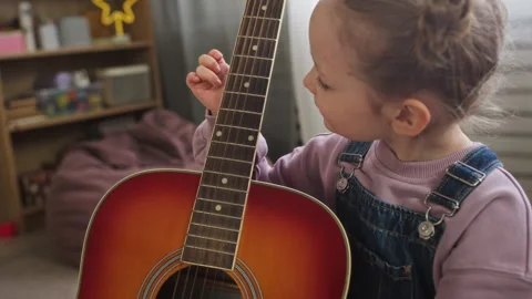 Focused Girl Touching Guitar Strings during Music Lesson at Kindergarten Stock Footage 332322218