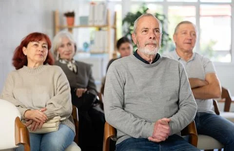 Focused group of students of different ages sitting on chairs and listening Stock Photos
