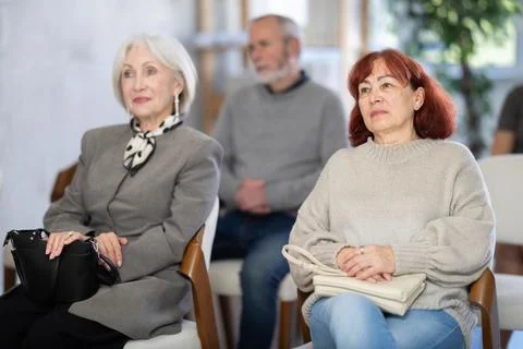 Focused group of students of different ages sitting on chairs and listening Stock Photos