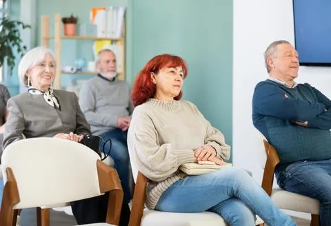 Focused group of students of different ages sitting on chairs and listening Stock Photos