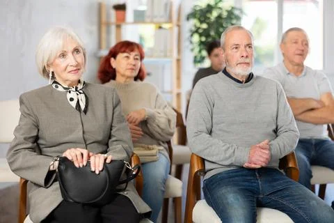 Focused group of students of different ages sitting on chairs and listening Stock Photos
