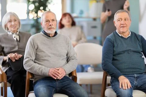 Focused group of students of different ages sitting on chairs and listening Stock Photos