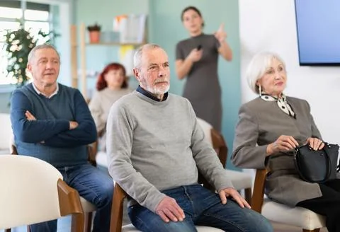 Focused group of students of different ages sitting on chairs and listening Stock Photos