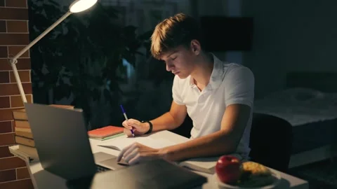 Focused guy typing on a laptop doing homework at his night study desk. Stock Footage 345208176