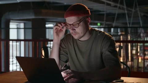 A focused hacker man is sitting working on a laptop in a dark room Stock Footage 260718916