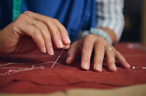 Focused hands sew rust-colored fabric with a needle and white thread during.. Stock Photos