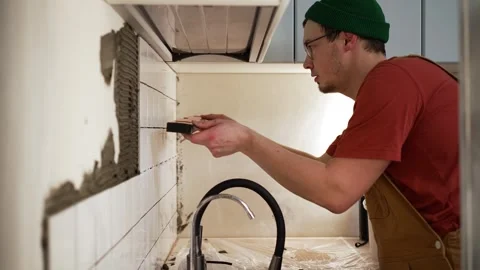 Focused handyman installing ceramic tile backsplash with cement adhesive during Stock Footage 344566672