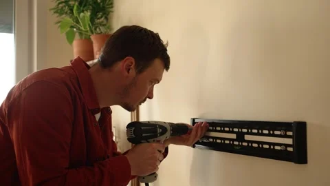 Focused handyman using a power drill for installing a television mount on a Stock Footage 344255301