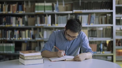 Focused high school student writing notes at desk in library in college Stockbeeldmateriaal 80523200