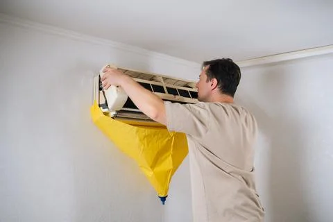 Focused HVAC technician carefully disassembling air conditioning unit, using Stock Photos