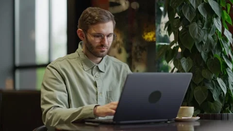 Focused Individual Engaged in Laptop Work at a Cozy Cafe Setting Surrounded by 库存影片 344799786
