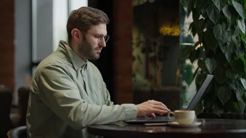 Focused Individual Engaged in Remote Work at a Cozy Coffee Shop, Typing on Stock Footage 344799899