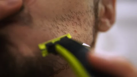 Focused individual meticulously trims beard using razor in bathroom setting Stock Footage 325614200