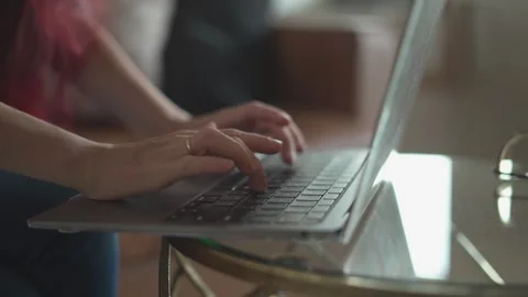 A focused individual is sitting comfortably while typing on their laptop in a Stock Footage 289965994