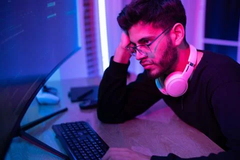 Focused individual working on a computer in a vibrant, neon-lit room during.. Stock Photos
