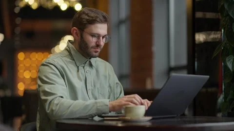Focused Individual Working on a Laptop in a Cozy Cafe Environment, Surrounded 库存影片 344799847