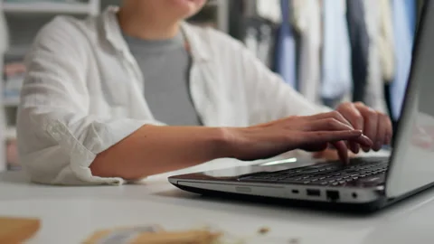 Focused individual working on a laptop at a tidy desk with fabric samples ne Stock Footage 323717763