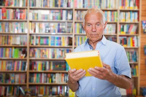 Focused intelligence elderly man choosing book in bookshop Stock-Fotos