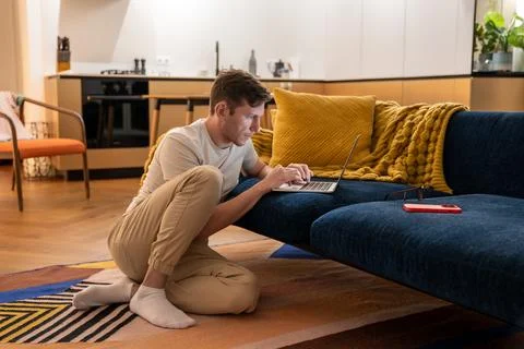 Focused IT guy sitting on floor with laptop working at home testes software Stock Photos