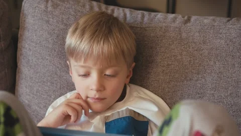 Focused little boy using a digital tablet on a couch at home Vídeos de archivo 347099495