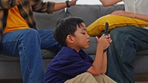 Focused little boy using mobile phone while parents at odds on sofa in Stock Footage 335179538