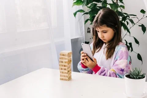 Focused little girl recording video or take photo of board game with wooden b Stock Photos