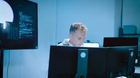 Focused male developer analyzing code on multiple desktop monitors in a mod.. 스톡 동영상 337027739