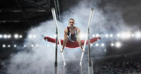 Focused male gymnast performing splits on parallel bars in arena Stock Photos