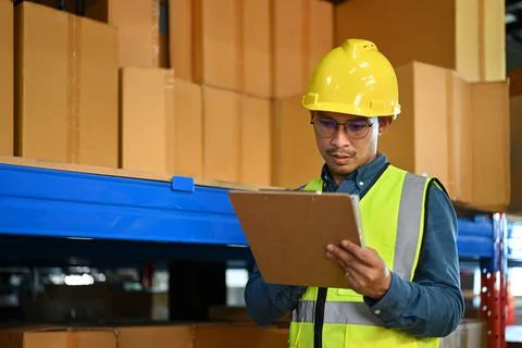 Focused male manager checking quantity of storage product while standing aisle Foto stock