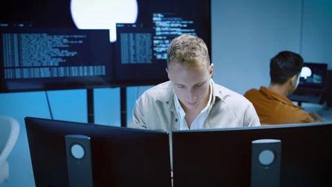 Focused male software engineer analyzing code on multiple monitors in a mod.. Stock Footage 337028811