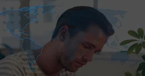 Focused man analyzing world data at office desk, with potted plant and map ov Stock Photos