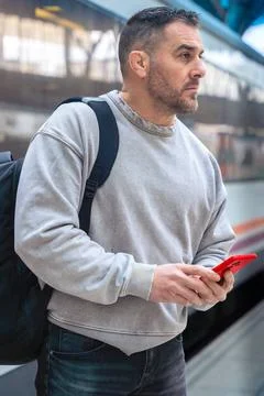 Focused Man with Backpack Using Smartphone at Train Station.Vertical Stock Photos