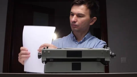 Focused man carefully preparing a classic mechanical typewriter by inserting Stockbeeldmateriaal 321621358