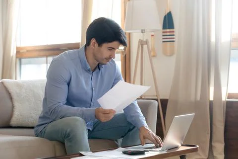 Focused man checking financial documents, using laptop, planning budget Fotos de archivo