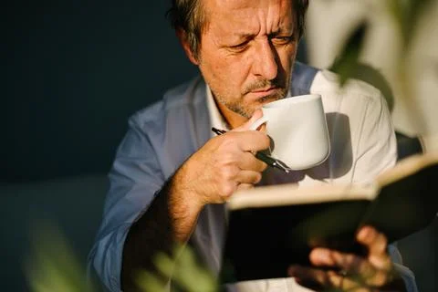 Focused man drinking coffee while reviewing notes in an open notebook under.. Stockfoto's