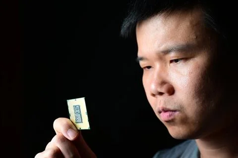 Focused man examining computer processor chip in hand under dramatic lighting 写真素材