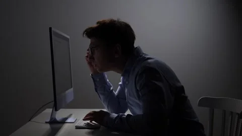Focused man in glasses working at a computer in a dimly lit office Stock Footage 342671829