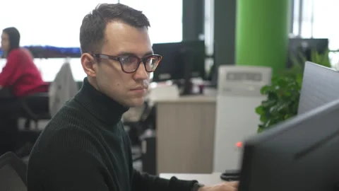 Focused man with glasses writes code on computer in office Stock Footage 325996274