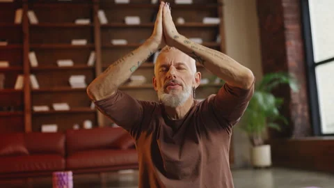 Focused man in his 50s sitting in lotus pose and meditating during yoga practice Stock Footage 340902080