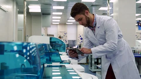 Focused man interacts with tablet near advanced laboratory machinery Stock Footage 311674536