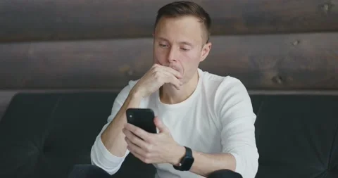 Focused man looks at the screen of smartphone that he holds in his hands while Stock Footage 197816449