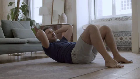 Focused man lying on floor and doing abs exercises Stock Footage 229635362