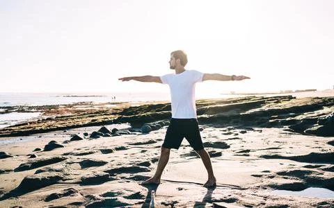 Focused man in process of doing Warrior pose at seaside Stock Photos