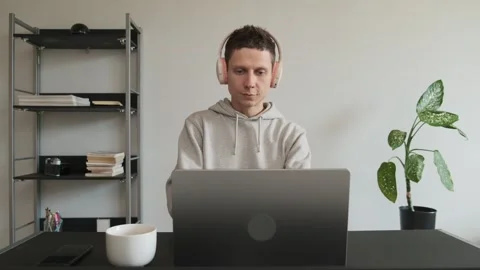 Focused man putting on headphones while working on laptop at home office desk Stock-Footage 308706984