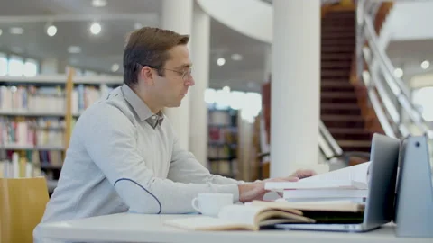 Focused man sitting at desk and writing in library Stock-Footage 232621506