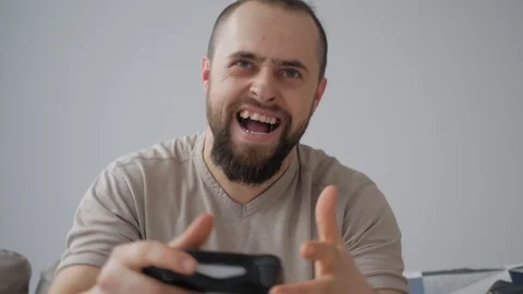Focused man sitting on sofa, holding joystick and playing video game, smiling an Stock Footage 125863522