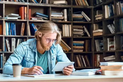 Focused man student using digital tablet make notes study online in library. Stock Photos