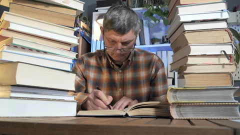 Focused man studying at desk surrounded by tall stacks of books 库存影片 334325680