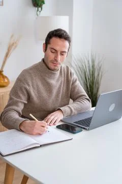 Focused man taking notes while working on laptop Stock Photos