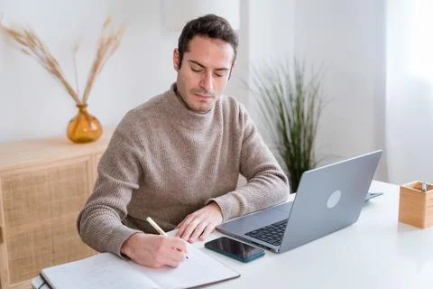 Focused man taking notes while working on laptop Foto stock